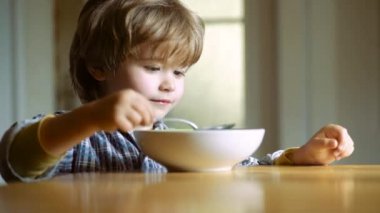 Evde sağlıklı yemek yiyen bir çocuk. Mutfakta kahvaltı eden küçük bir çocuk. Mutlu erkek bebek kaşık kendini yiyor. Mutfakta bebek yeme yemeği.