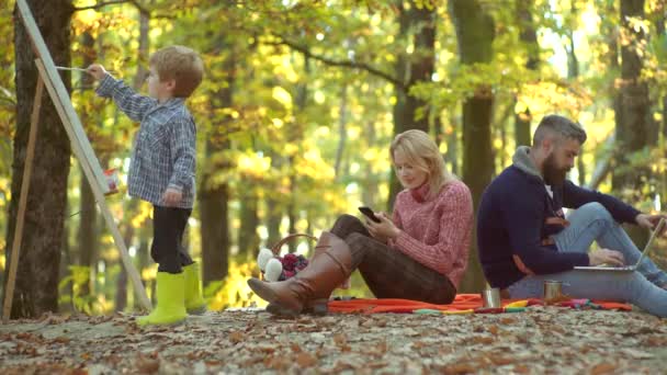 黄色い自然の中で一緒に幸せな家族。秋の葉に横たわる小さな息子と幸せな笑顔の若い両親。秋の自然に絵を描く幸せな子どものアーティスト. — ストック動画