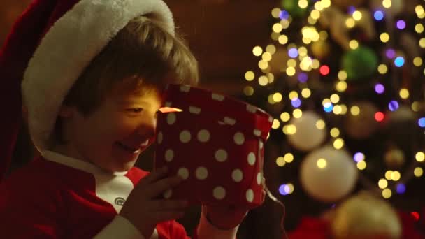 Gelukkig schattig kind in Santa hoed met heden hebben een kerst. Vrolijk schattig kind het openen van een kerstcadeau. Winter Kerst emotie. Little Santa Claus feest cadeaus cadeau. — Stockvideo