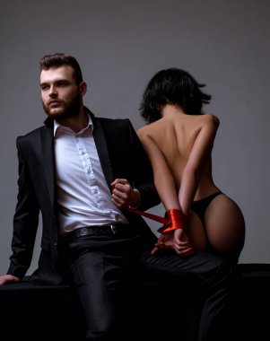Seksi kız çıplak kalça. Tutkulu aşıklar. Seks hakimiyeti. Seks teslimiyeti. Maço bakımlı hipster ve çıplak seksi kadın elleri kırmızı kurdele bağlı. Cinsel ilişkiler. Seks oyunu. Tease ve baştan