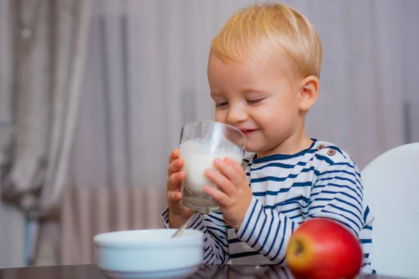 Comida saludable. Niño lindo bebé desayunando. Nutrición del bebé. Come sano. Un niño comiendo bocadillos. Nutrición saludable. Bebe leche. El niño sostiene un vaso de leche. Niño lindo chico sentarse a la mesa con plato y comida — Foto de Stock