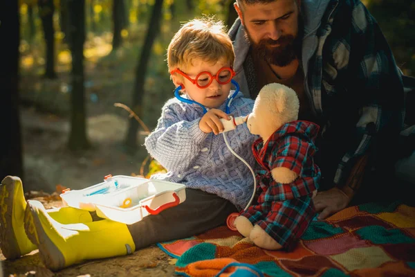 Çocuk çocuk baba doğa arka plan ile doktor oynamak. Temiz havada oyunlar. Stetoskoplu gözlüklü doktor çocuk hastayı muayene eder. Doktor üniformalı çocuk hastayı tedavi edin. Eğitim yetiştirme ve geliştirme — Stok fotoğraf