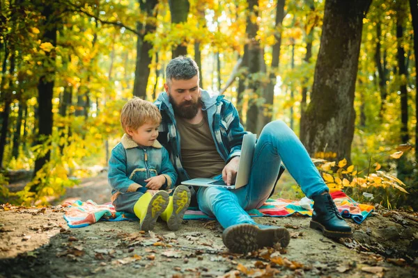 Hombre barbudo padre e hijo pequeño con portátil en el bosque. Educación ecológica. Padre enseña al hijo a usar la tecnología moderna. Unidos con la naturaleza. Lección de ecología. Escuela forestal y educación ecológica — Foto de Stock