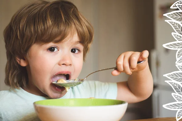 En sulten liten gutt som spiser. Et muntert lite barn spiser selve maten med skje. Velsmakende barnefrokost. Baby spiser mat på kjøkkenet. Lykkelig gutt spiser sunn mat skje i seg selv. – stockfoto