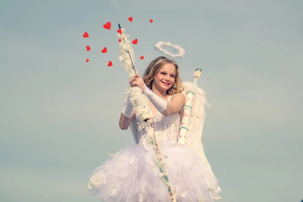 Pijl van de liefde. Portret van een cupido meisje. Leuke tiener cupido op de wolk - lucht achtergrond. onschuldig meisje met engelenvleugels met pijl en boog tegen blauwe lucht en witte wolken — Stockfoto