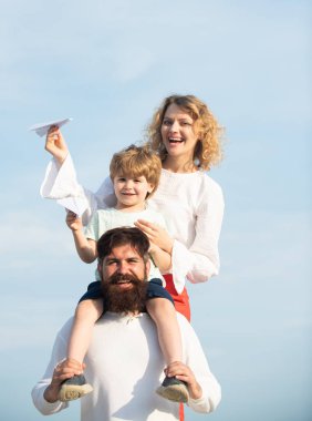Baba anne ve oğlu dışarıda oynuyorlar. Yaz istihkakı. Sevimli küçük çocuk kağıt uçak tutuyor. Mutlu bir aile. Ebeveynler ve çocuk. Mutlu aile ve küçük oğlu mavi yaz gökyüzünde oynuyor.