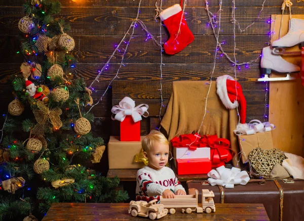 Lächelndes Kind, das hinter dem Weihnachtsbaum im Wohnzimmer hervorlugt. niedliches kleines Kind in der Nähe des Weihnachtsbaums. fröhliches süßes Kind, das ein Weihnachtsgeschenk öffnet. christmas kids - Glückskonzept. — Stockfoto