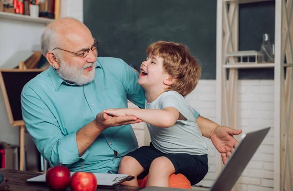 Portrét sebevědomého starého učitele mužského. Světový den učitelů. Šťastný roztomilý vnuk a dědeček sedí u stolu vevnitř. Vzdělávací proces. Dědeček s vnukem spolu. — Stock fotografie