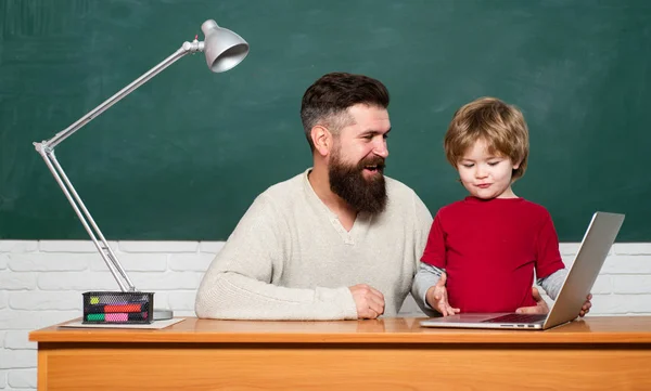 Teacher and kid. father teaching her son in classroom at school. Daddy and son together. Happy family - daddy and son together. Teacher and schoolboy using laptop in class.