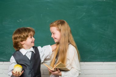 Sınıfta bir çift küçük kız ve oğlan. Okula geri dön. Tahtada neşeli gülümseyen çocuk. Eğitim. Öğretmen kız öğrenci ders ile liseli yardım. Okul dersleri.