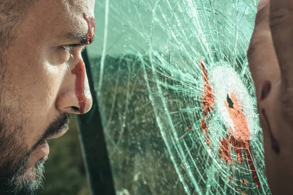 Surviving an injury. Latino man with wound injury looking through broken glass. Hispanic man bleeding from head injury. Handsome injured guy with skin deep injury — Stock Photo, Image