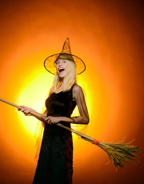 Festa de Halloween sexy e abóbora engraçada. Retrato interno de bruxa jovem bonito na festa de Halloween. Retrato de uma bruxa loira linda em vestido preto e um chapéu com abóbora sobre fundo laranja . — Fotografia de Stock