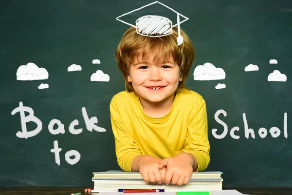 Happy school kids. School concept. Classroom. Funny little boy pointing up on blackboard. School kids against green chalkboard.