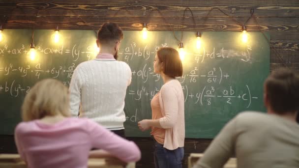 Teenageři mladý tým společně veselý koncept. Dívka studuje matematické vzorce v blízkosti desky s učitelem, zadním výhledem. Skupina dospívajících studentů spolupráce na projektu. Vousatý učitel. — Stock video