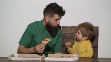 Erkek ve çocuk beyaz üzerine izole pizza yer. Mutlu baba çocuk çocuğun pizza yediği portresi. Mutlu bir aile tahta masada pizza yiyor. Beyaz üzerine izole edilmiş. Arka plan. Sevimli çocuk ile sakallı adam.