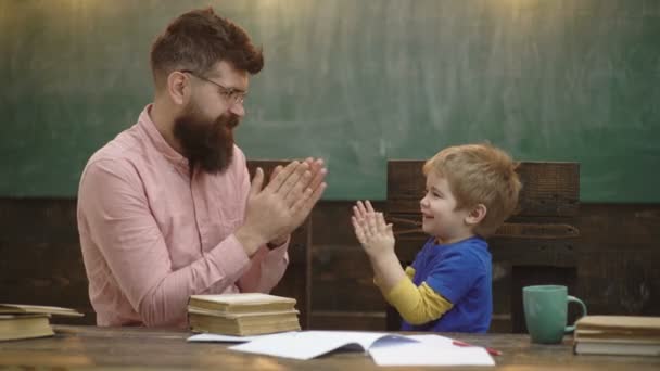 Mann und Junge machen Übungen im Klassenzimmer, sitzen auf einem Tisch im Hintergrund auf einer Kreidetafel. Kind lernt mit Lehrer. Vater bringt Sohn bei, diskutiert, erklärt. Bildungskonzept. Grundschulbildung. Hintergrund. — Stockvideo