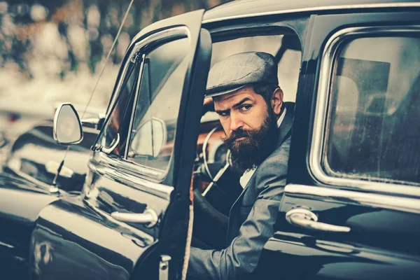 Confident wealthy young man with beard in classic car.