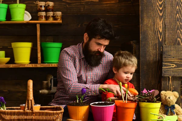 Father and son. Fathers day. Flower care. Soil fertilizers. Family day. Greenhouse. bearded man and little boy child love nature. happy gardeners with spring flowers. Cheerful farmer in greenhouse