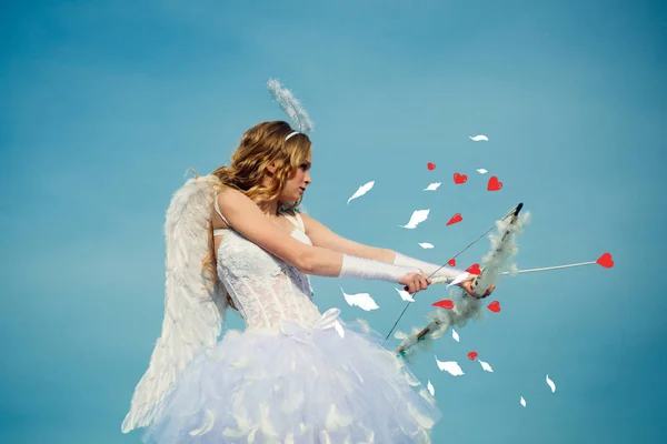 Niña ángel con alas blancas. Chica inocente con alas de ángel de pie con arco y flecha contra el cielo azul y nubes blancas. Adolescente ángel — Foto de Stock