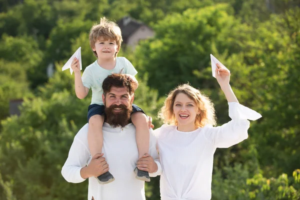 Enfant heureux avec des parents jouant avec des ailes de jouet sur fond de ciel d'été. Joyeux garçon souriant sur l'épaule papa regardant la caméra. Enfance. Mère père et fils . — Photo