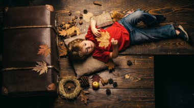 Sarışın küçük çocuk mide üzerinde yaprak ile istirahat sonbahar yaprakları ahşap zemin üzerinde yatıyor. Çocuklar için tüm sonbahar giysileri için en büyük indirimler. Yaprak sonbahar ile eğlenen çocuk.