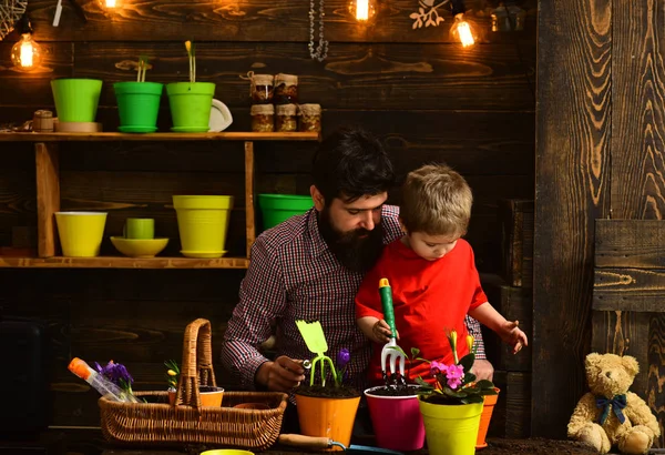 happy gardeners with spring flowers. Family day. Greenhouse. bearded man and little boy child love nature. Father and son. Fathers day. Flower care watering. Soil fertilizers. Fertile present