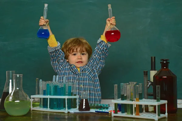 Iskolai koncepció. Oktatás. Vidám, mosolygós kisfiú, aki jól szórakozik a kék falon. Egy új kísérletet végeztek a kémiában. Óvodás vagyok. Gyerek az osztályteremben táblával a háttérben — Stock Fotó