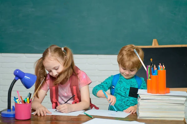 Torniamo a scuola e siamo felici. Il ragazzo sta imparando in classe sullo sfondo della lavagna. Carino piccolo bambino in età prescolare ragazzo con bambina in una classe . — Foto Stock