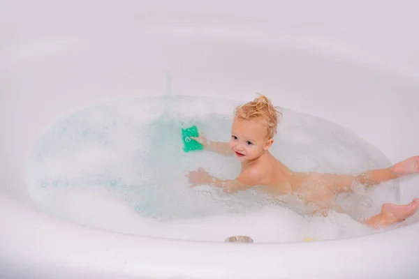 Niedlichen kleinen Jungen waschen. glücklich lachendes Baby, das ein Bad nimmt und mit Schaumblasen spielt. — Stockfoto