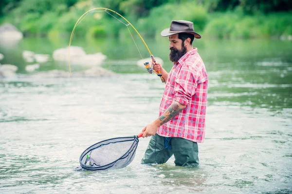 Tengo la trota fario. Uomo con canne da pesca sul molo del fiume. Uomini che pescano nel fiume durante la giornata estiva. Pescatore a mosca con canna da pesca a mosca nel bellissimo fiume . — Foto Stock