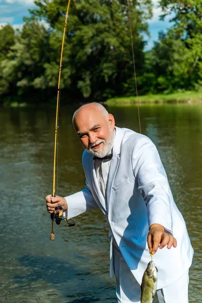 American angler fishing. Still water trout fishing. Handsome mature fisherman in white suit fishing in a river with a fishing rod. Fish on the hook.