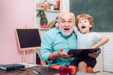 Okulda öğretmen ve öğrenci birlikte öğreniyor. Öğretmenler günü. Sınıfta tahtaüzerinde büyükbaba ve torunu portresi. Kendine güvenen yaşlı erkek öğretmenin portresi.