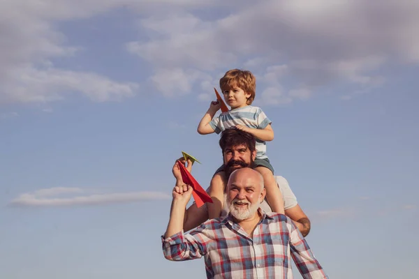 푸른 하늘과 구름 배경 위에 장난감 종이 비행기와 행복 할아버지 아버지와 손자. 세 남자 세대. 화창한 날에 간단한 종이 비행기로 노는 아이들. — 스톡 사진