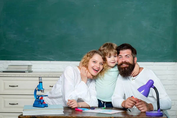 Junges Paar hilft seinem Sohn bei den Hausaufgaben. Lehrertag. Familientag. Schüler der Grundschule lernen drinnen. Kinder im Vorschulalter. Eltern sind stolz auf Fortschritte ihres Sohnes. — Stockfoto