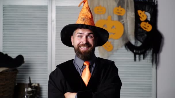 Festa de Halloween e feiticeiro engraçado. Dia das Bruxas. Chapéu mágico. O homem barbudo em um chapéu cor-de-laranja levanta sobrancelhas e faz emoções diferentes na cara. Feiticeiro alegre de chapéu. Homem barbudo emocional . — Vídeo de Stock