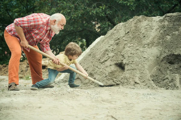 Ребенок и работа. Маленький сын рабочий с лопатой. Маленький сын помогает отцу со строительными работами. Концепция детства. Будущий работник сын с отцом . — стоковое фото