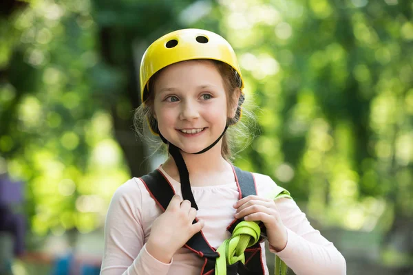 Nettes kleines Mädchen in Klettersicherheitsausrüstung im Baumhaus oder im Seilpark klettert auf das Seil. Sommeraktivitäten für Kinder. glückliches kleines Mädchen im Sommer. — Stockfoto
