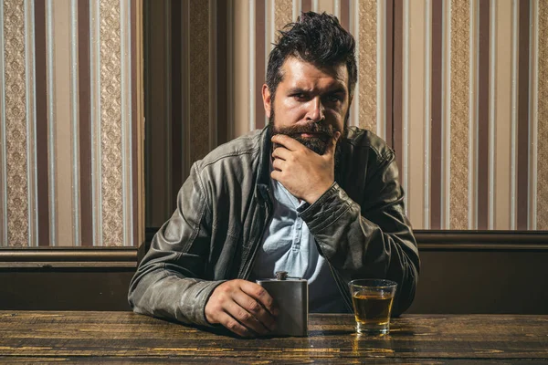 Man with beard holds glass brandy. Man holding a glass of whisky. Handsome stylish bearded man is drinking whiskey. Barbershop, shaving. Thinking to drink or not to drink. — Stock Photo, Image