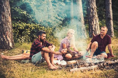İki çiftler ormanda kamp. Kamp ateşi üzerinde sosis pişirme erkekler. Esmer sarışın kızlar kucağına yalan yorgun