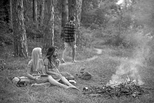 Fiatal lányok olvasás könyveket erdőben vagy parkban. Gyönyörű nők ülő mellett tábortűz. Guy sétál az ösvényen a fák — Stock Fotó