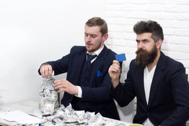 Sakallı yönetici ve nakit ve kart kavanozu olan iş arkadaşı. İş arkadaşları banka hesabı yerine kavanozda para topluyorlar. Nakit sorunları kavramı. İş ortakları ve işadamları ofiste buluşuyor