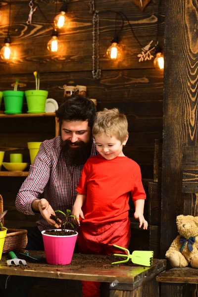 happy gardeners with spring flowers. bearded man and little boy child love nature. Flower care watering. Soil fertilizers. Family day. Greenhouse. Father and son. Fathers day. Revel in beauty
