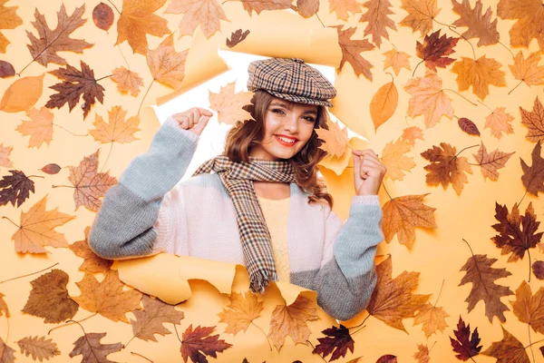 Perfect fashion accessories for autumn. Pretty woman wear autumn fashion accessories. Casual fashion trends for fall. Fashion girl look through torn paper with autumn leaves. Fall look of vogue model