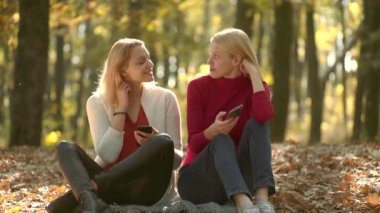 Sonbahar parkında telefonu olan kızlar bekliyor. Akıllı telefon kullanan iki kız. Çevrimiçi sohbet. Konuş benimle. Livechat Sohbet İletişim konsepti. Genç blogcular, blog konsepti.