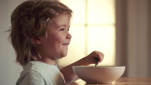 Retrato de un hermoso niño desayunando en casa. Sabroso desayuno para niños. Niño sentado en la mesa comiendo comida saludable con expresión divertida en la cara . — Vídeos de Stock