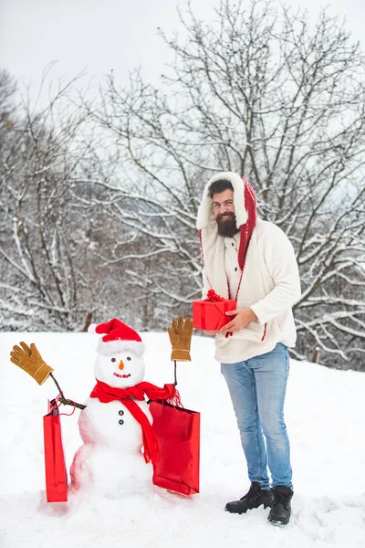 Feliz hombre de nieve sonriente en el soleado día de invierno con el padre feliz. Lindo muñeco de nieve y barbudo con bolsa de compras. Muñeco de nieve divertido con bolsa de compras - descuento y concepto de venta de invierno . — Foto de Stock