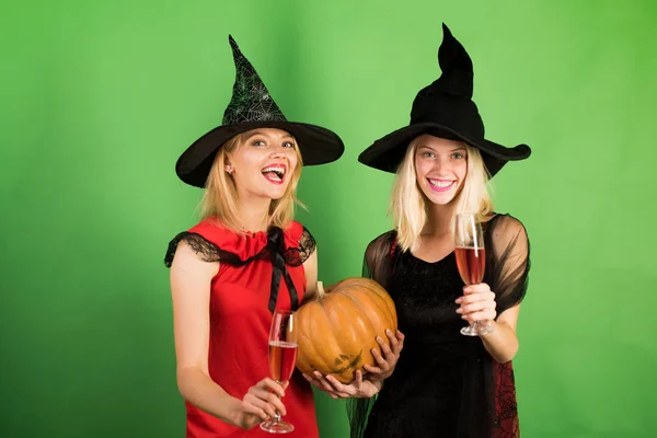 Две счастливые молодые женщины в черно-красных платьях, костюмы ведьм Хэллоуин на вечеринке на зеленом фоне. Праздничный дизайн на Хэллоуин. Две красивые блондинки в карнавальных костюмах . — стоковое фото