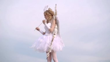ok ve kanatlar. Genç Cupid. Mutlu genç melek kız. Gökyüzü arka planı ndaki bir meleğin kıyafetlerini giymiş bir çocuk. Metin için boşluk. Tatlı melek kız
