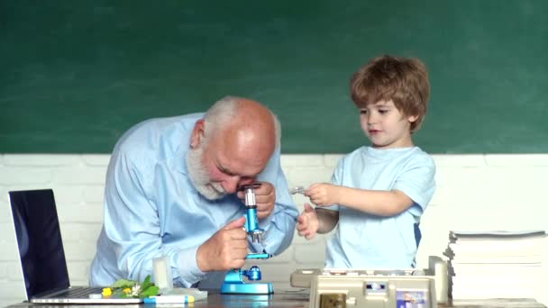 Emeklilik yaşı kavramı. Kendine güvenen yaşlı erkek öğretmenin portresi. Dünya Öğretmenler Günü. Mutlu sevimli Torun ve Büyükbaba kapalı bir masada oturuyor. Eğitim süreci. — Stok video