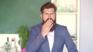 Okulda ki sakallı profesör sınıftaki masalarda. Okul konsepti. Ciddi erkek öğrenci okulda okuyor. Okul sınıfında tebeşir tahtası yakınında genç sakallı öğretmen.